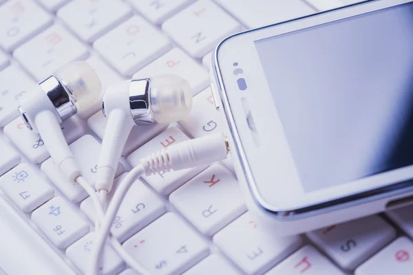 Biały smartphone rezygnować słuchawki na klawiaturze — Zdjęcie stockowe