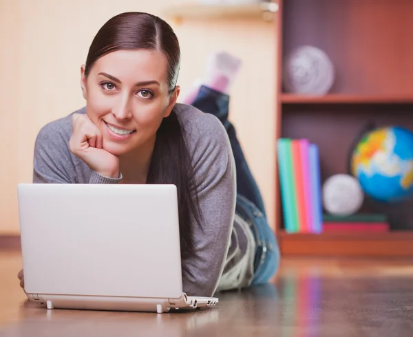 Mosolygó fiatal nő feküdt fa padlóburkolatok, laptop — Stock Fotó