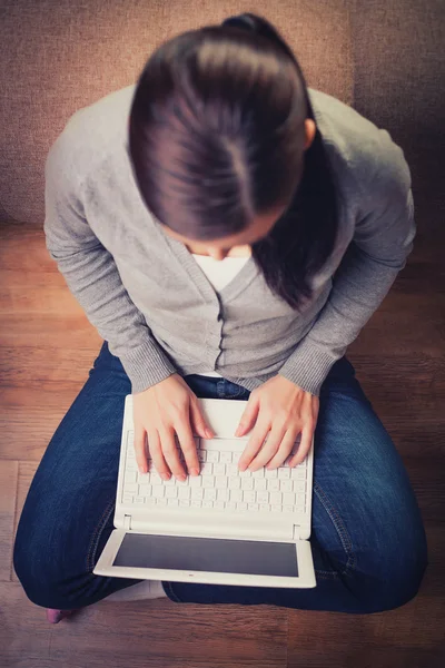 Mulher está sentada no chão de madeira com laptop — Fotografia de Stock