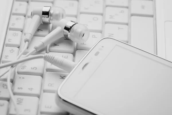 Biały smartphone rezygnować słuchawki na klawiaturze — Zdjęcie stockowe
