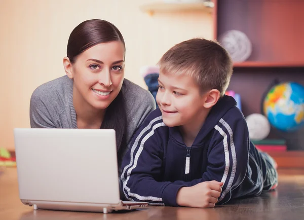 Mom and son are lying on wood floor with laptop — Stockfoto