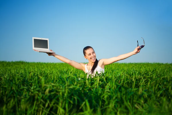 Молодая женщина с ноутбуком сидит на зеленой траве и смотрит в небо — стоковое фото