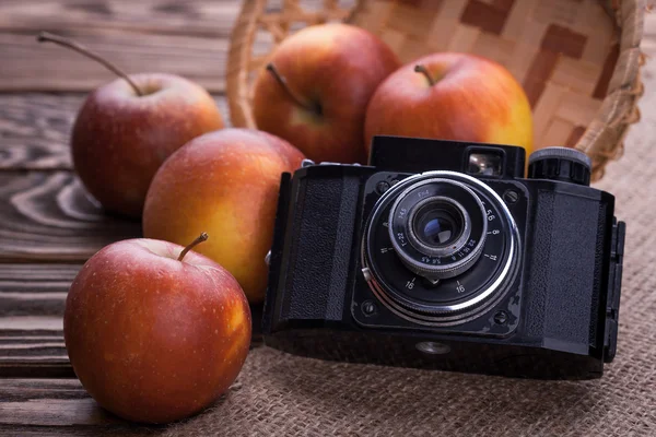 Retro fotoaparát a červená jablka na dřevěný stůl — Stock fotografie
