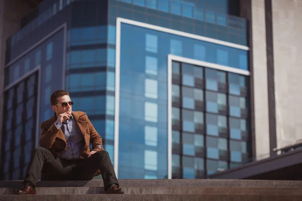 Handsome man is sitting on a skyscraper background — Stock Photo, Image