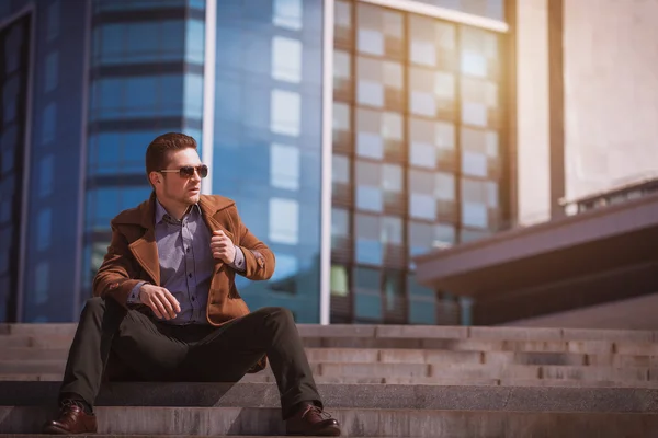 Handsome man is sitting on a skyscraper background — Stock Photo, Image