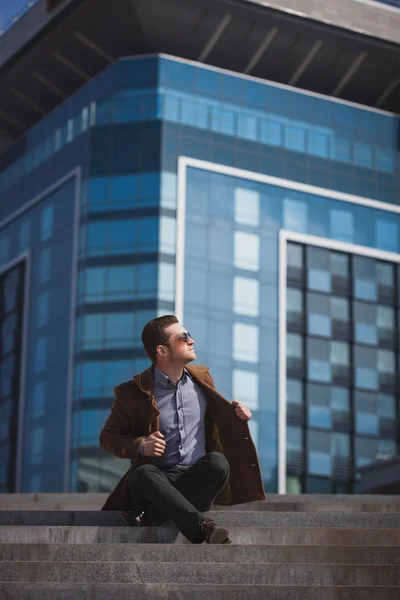 Hombre guapo está sentado sobre un fondo de rascacielos — Foto de Stock