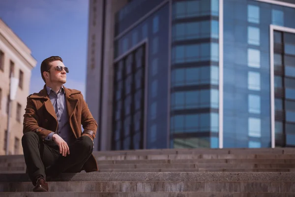 Handsome man is sitting on a skyscraper background — Stock Photo, Image