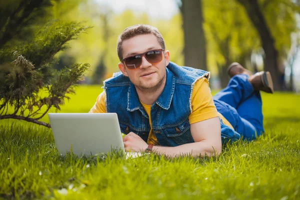 Ung man i parken ligger på gräset med laptop — Stockfoto