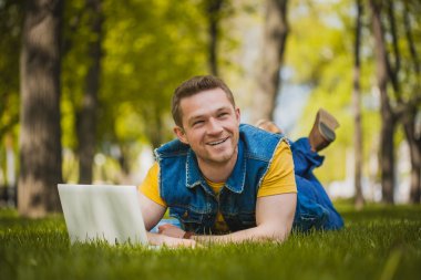 genç adam parkta laptop ile çim üzerinde yalan