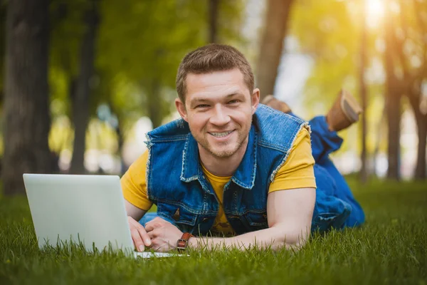 Молода людина в парку лежить на траві з ноутбуком — стокове фото