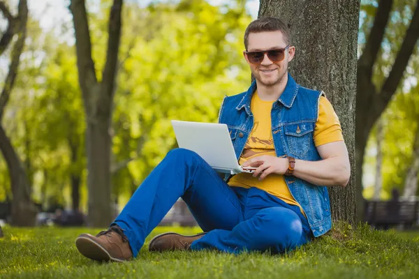 Ung man i parken med laptop — Stockfoto