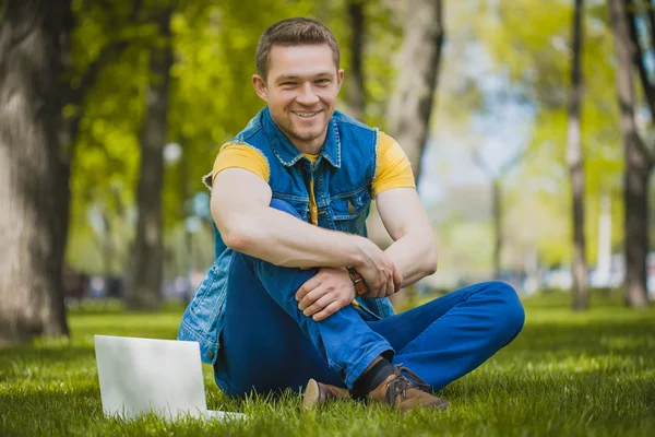 ラップトップと草に横たわって公園で若い男 — ストック写真