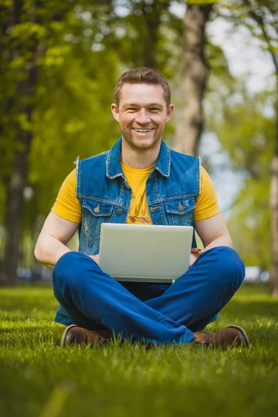 Молода людина в парку лежить на траві з ноутбуком — стокове фото