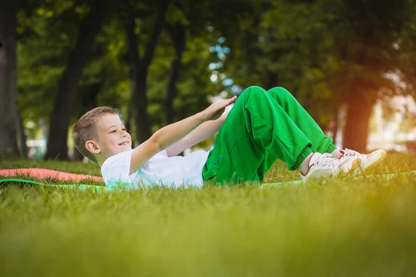 Happy kid is doing exercises in the park — Stock Photo, Image