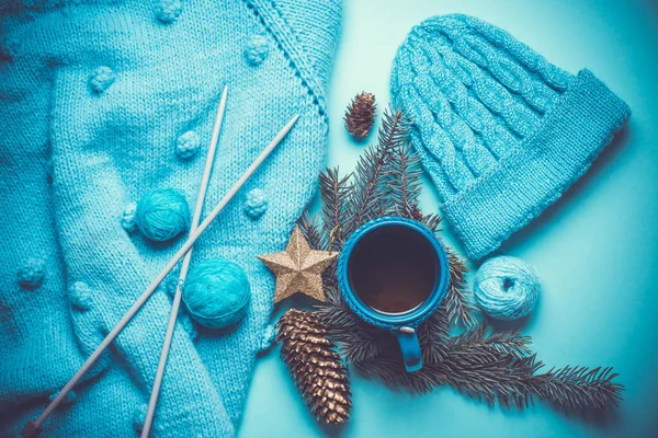 Ręcznie robiony niebieski sweter, ciepły dzianinowy kapelusz, gorąca filiżanka herbaty, choinka i wystrój noworoczny, na starym drewnianym tle — Zdjęcie stockowe