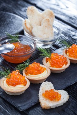 Tereyağlı tartlar, kırmızı havyar ve siyah ahşap bir masada dereotlar..