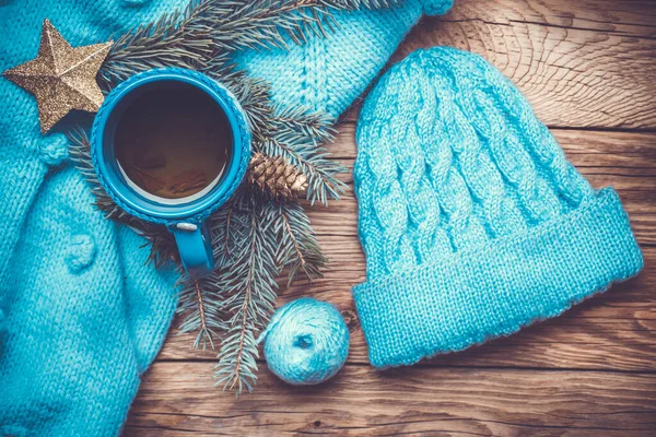 Ręcznie robiony niebieski sweter, ciepły dzianinowy kapelusz, gorąca filiżanka herbaty, choinka i wystrój noworoczny, na starym drewnianym tle — Zdjęcie stockowe