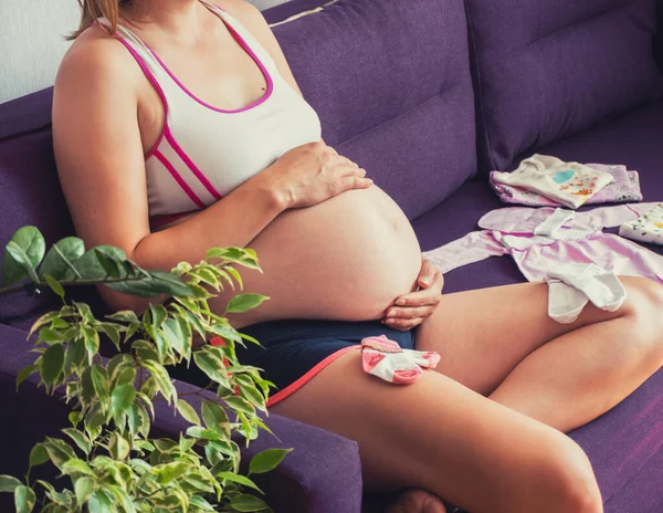 妊娠中の女性はソファに座って家で腹を触っていました。新生児を待って. — ストック写真