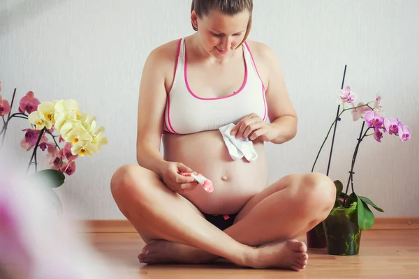 Mujer embarazada sentada en el suelo con flores de orquídea en casa. esperando al recién nacido. — Foto de Stock