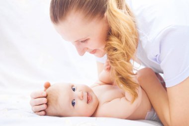 Genç mutlu anne ve yeni doğmuş bebeği beyaz bir yatakta neşeyle yatıyor.