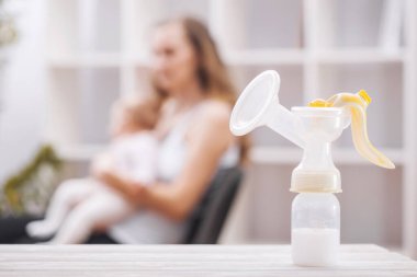 Annenin elinde tuttuğu anne sütünün arka planında elle yapılan göğüs pompası. Annelik ve bebek bakımı.