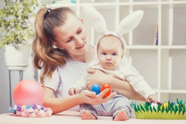 Mutlu anne ve bebek tavşan kulaklı Paskalya yumurtası oynuyorlar.