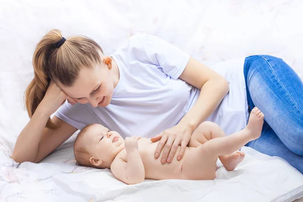 Genç mutlu anne ve yeni doğmuş bebeği beyaz bir yatakta neşeyle yatıyor. — Stok fotoğraf