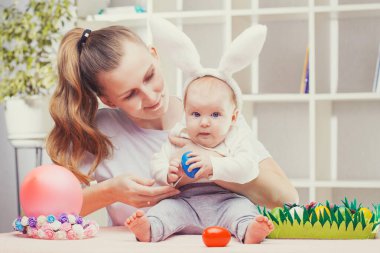 Mutlu anne ve bebek tavşan kulaklı Paskalya yumurtası oynuyorlar.