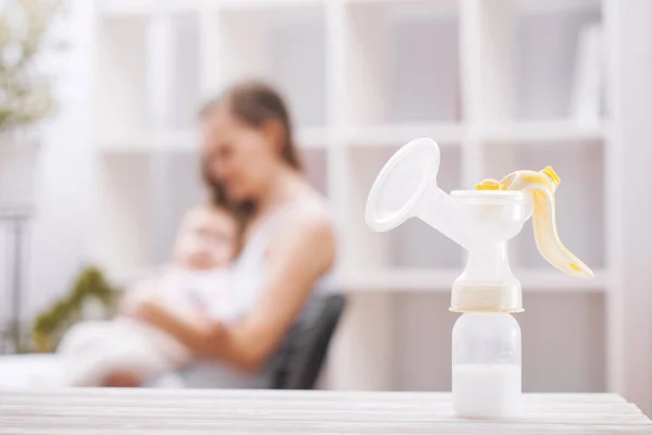 Tiralatte manuale con latte materno sullo sfondo della madre che tiene in mano il bambino. — Foto Stock
