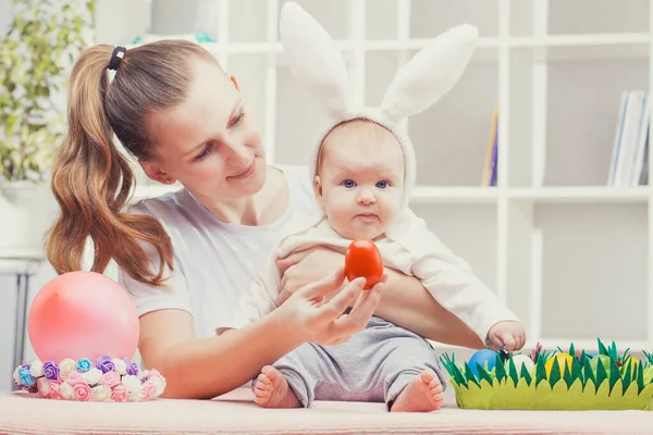 Счастливая мать и ребенок с ушами кролика играют в пасхальное яйцо. — стоковое фото