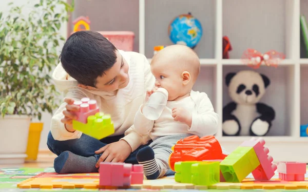 Older brother plays with sister with colourful building blocks at home or kindergarten — Stok fotoğraf