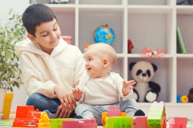 older brother plays with sister with colourful building blocks at home or kindergarten
