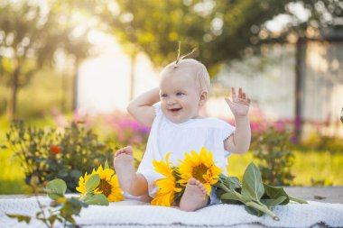 cute one year old baby girl in a blooming garden with a bouquet of sunflowers