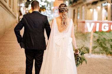 Düğün kıyafetleri içinde bir çift gece sokakta yürüyorlar.