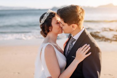 Gün batımında sahilde öpüşen evli bir çift.