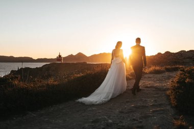 Gün batımında deniz fenerine doğru yürüyen evli bir çift.