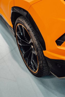 Detail of the rear wheel of an orange sports car where you can see a white background