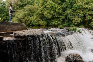 Ormanın yakınındaki şelalenin üstünde duran bir kadın.