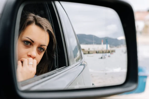 Mirror portrait of a young woman sitting on the passenger seat of a car