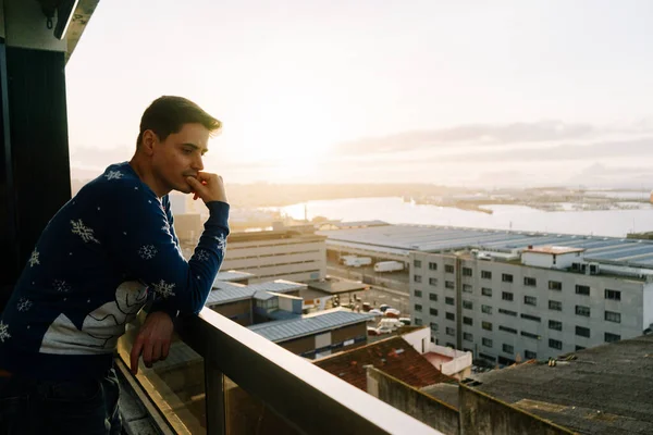 Man contemplating an industrial city from a balcony at sunset, with the sea and the sky