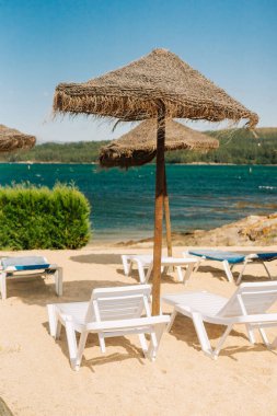 Deck chairs with straw parasols near the river in Galicia, Spain