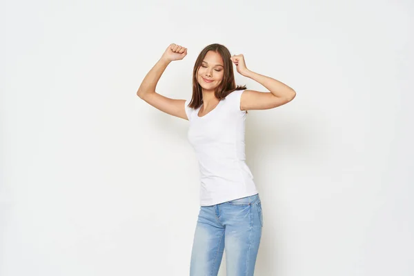 Νεαρή γυναίκα σε ένα λευκό t-shirt χειρονομίες με τα χέρια της σε ένα ελαφρύ φόντο τζιν μοντέλο — Φωτογραφία Αρχείου