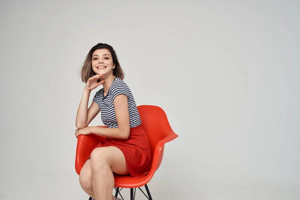 Hermosa mujer en una camiseta a rayas sentado en la silla roja peinado de estilo moderno —  Fotos de Stock