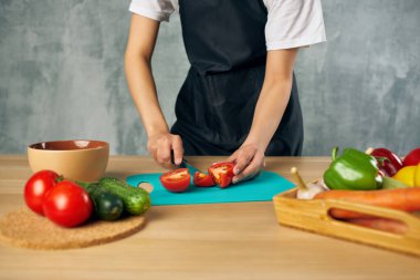 Ev hanımı mutfakta sebze kesme tahtası kesiyor.