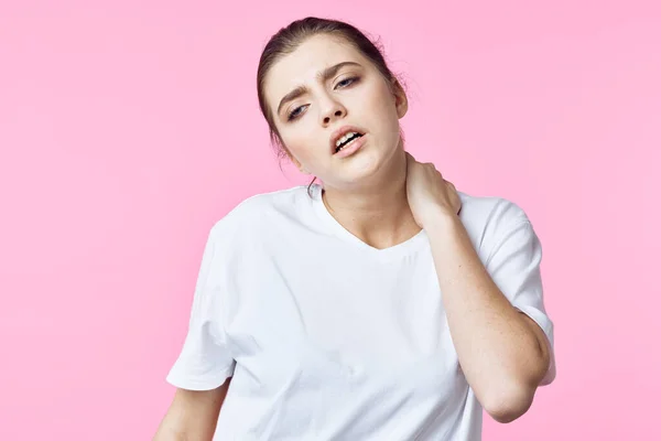 Mulher em t-shirt branca segurando seu pescoço problemas de dor fundo rosa — Fotografia de Stock