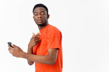 Cep telefonu Afrika görünümlü mutlu adam turuncu tişört ışık arka plan