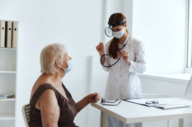 Doktor sağlık kontrolünde tıbbi maske takan yaşlı bir kadın.