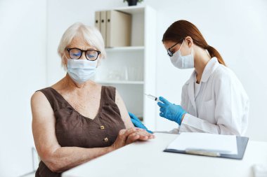 Aşılar için hastanede maske takan yaşlı bir kadın var.