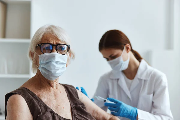 Stará žena v lékařské masce sedí vedle pasu zdravotní sestry vakcíny — Stock fotografie