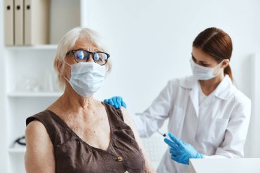 Aşılar için hastanede maske takan yaşlı bir kadın var.